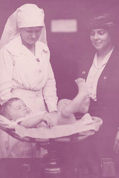 Sister Muriel Peck weighs a baby while proud mother looks on. Courtesy of the State Library of Victoria.