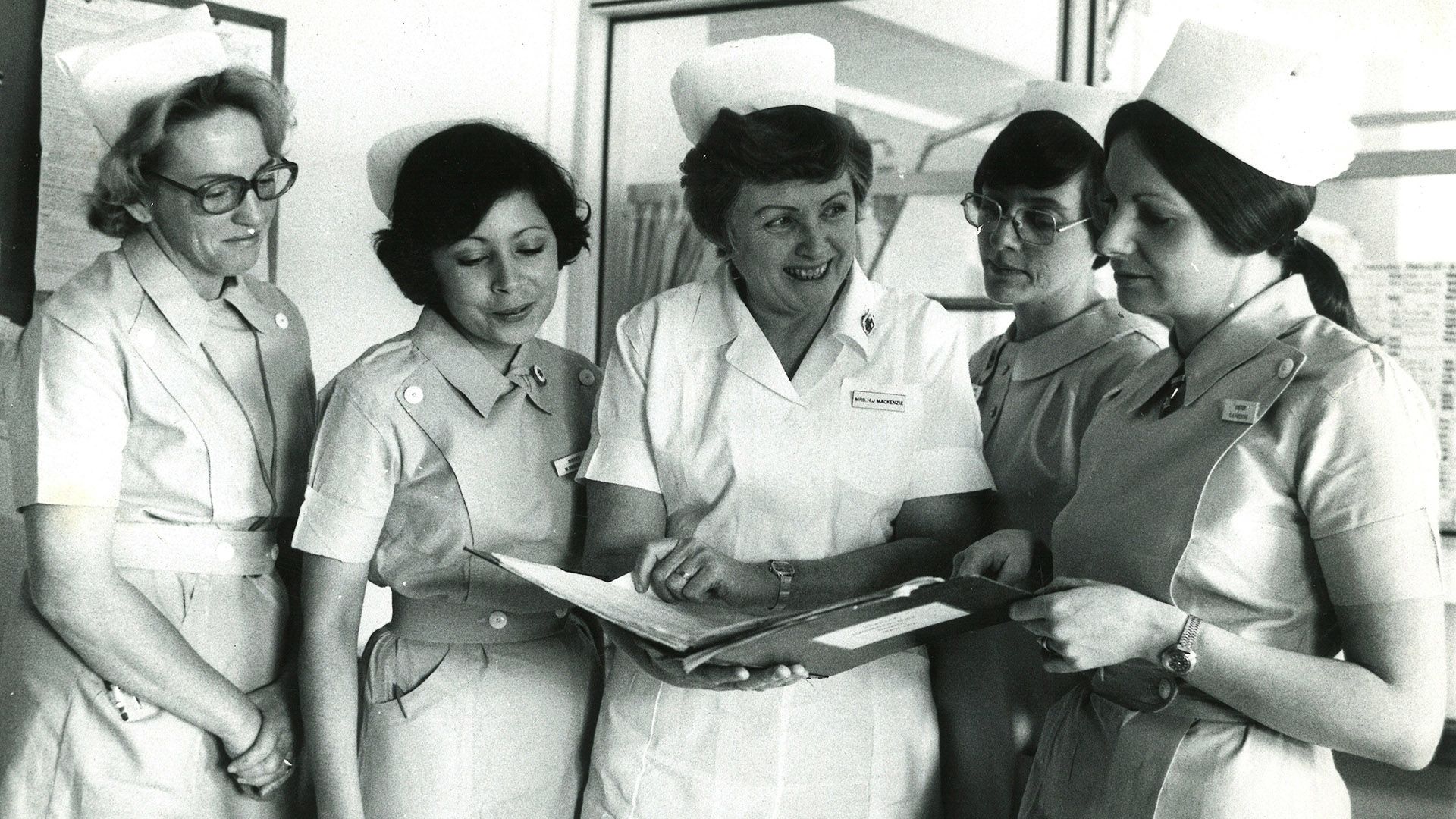 Five nurses in uniform looking at a folder held by the nurse in the centre